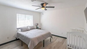 A bedroom with a bed, a crib, a ceiling fan, and a window with blinds. - Close to Kyle Field, Texas A&M, Santa’s Wonderland & anywhere you need. (College Station)