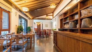 A restaurant with wooden furniture, a tiled floor, and a ceiling with wooden beams and pendant lights. - Jiu Hua Qing Quan Hotel (Qingyang)
