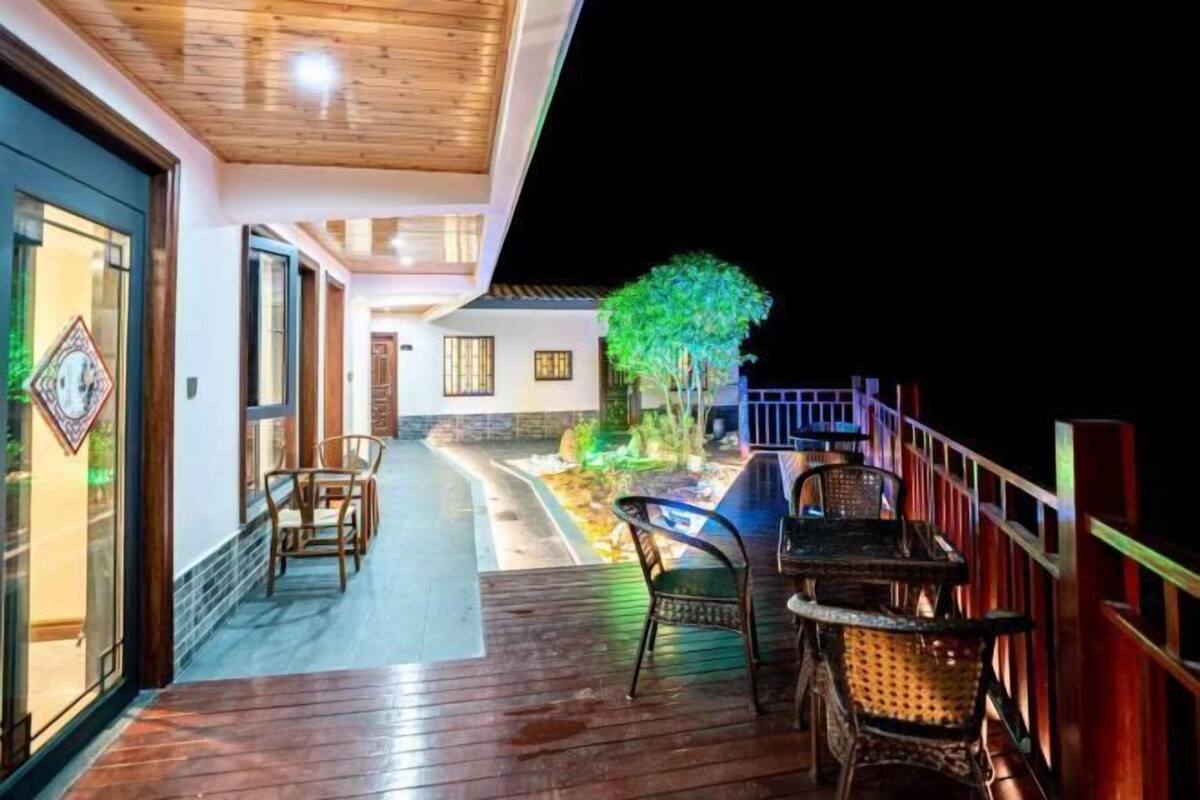 A wooden deck with outdoor seating, a pathway leading to a building, and a tree illuminated at night.