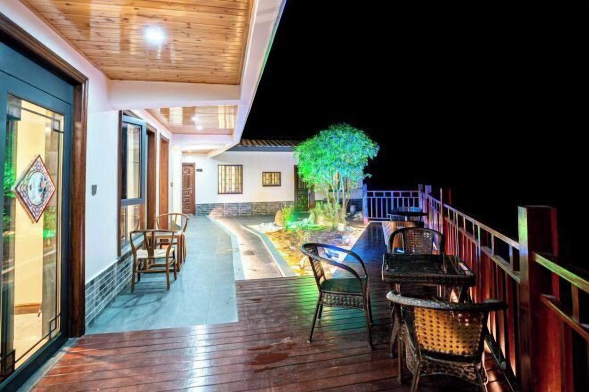 A wooden deck with outdoor seating, a pathway leading to a building, and a tree illuminated at night.