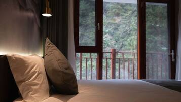Un dormitorio con una cama grande, dos almohadas, una mesita de noche y una ventana con vistas a árboles.