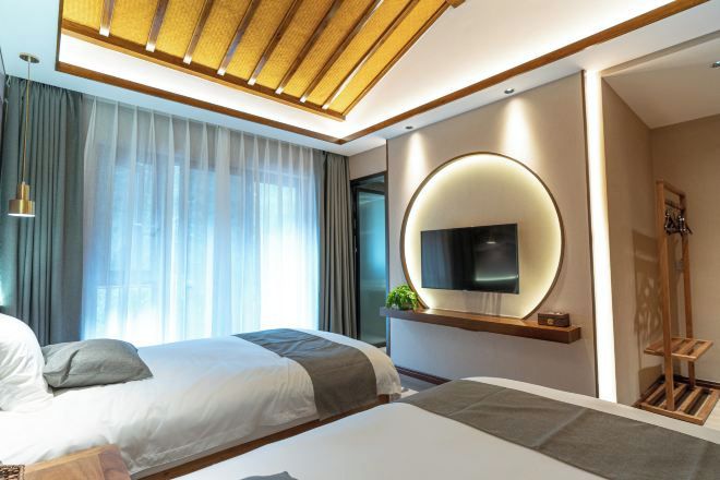 Una habitación de hotel moderna con dos camas, un televisor grande montado en la pared y un techo con listones de madera.