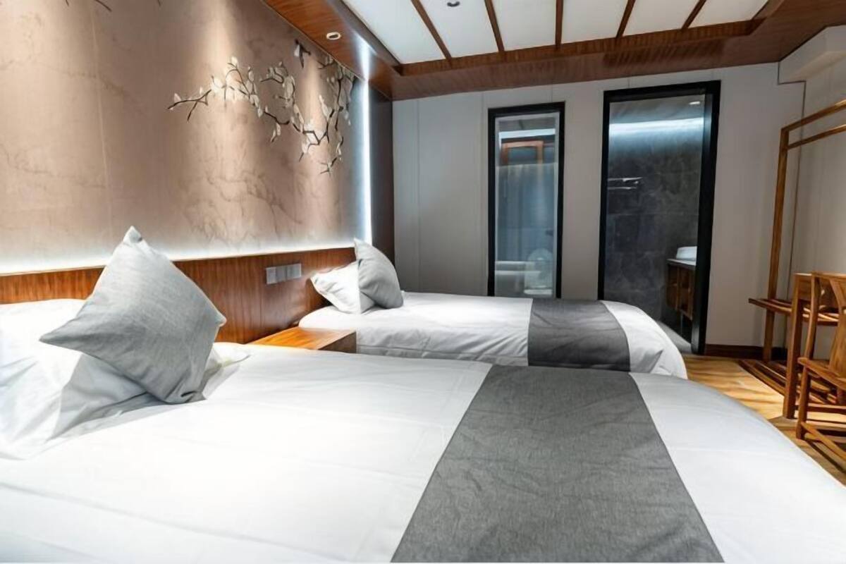 A hotel room with two beds, a wooden headboard, a wall-mounted decorative piece, and a sliding door leading to a bathroom.