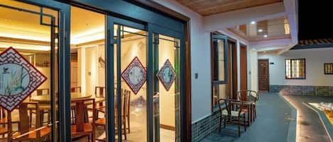 Un edificio moderno con amplios ventanales, una terraza de madera y un área de comedor con sillas y mesas.