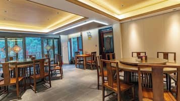 A dining area with wooden tables and chairs, a tiled floor, and a modern ceiling design.