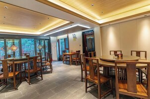 Un comedor con mesas y sillas de madera, piso de baldosas y un diseño moderno en el techo.