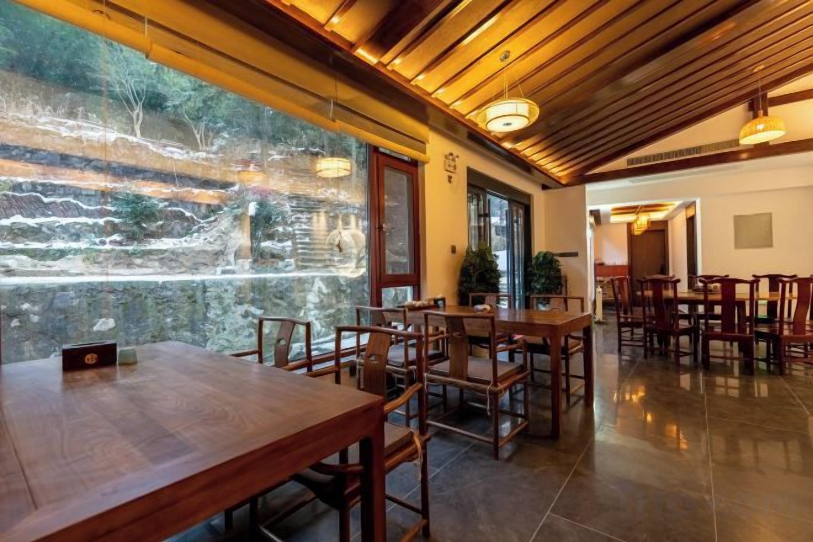 A restaurant with wooden tables and chairs, a view through a glass wall, and a tiled floor.
