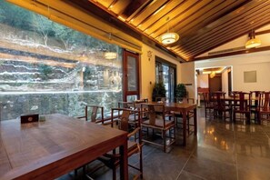 Un restaurante con mesas y sillas de madera, vistas a través de un ventanal y suelo de baldosas.