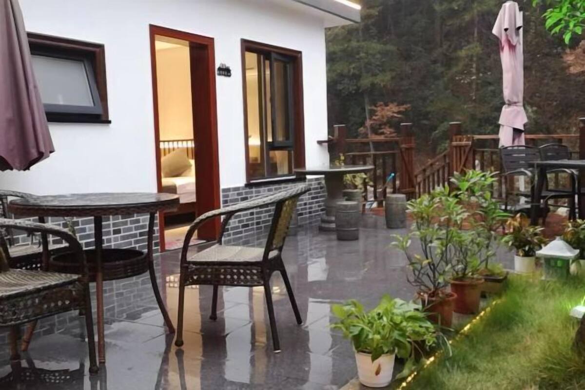 A patio with outdoor seating, a white building with a wooden door, and potted plants.