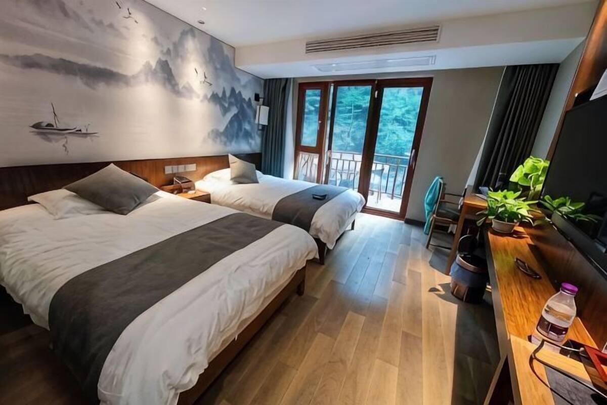 A hotel room with two beds, a desk, a TV, and a balcony with a view.