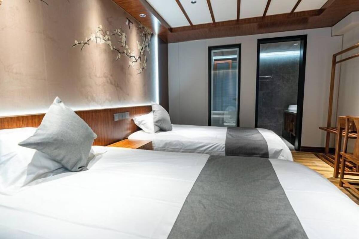 A hotel room with two beds, a wooden headboard, a wall with a textured design, and a door leading to a bathroom.