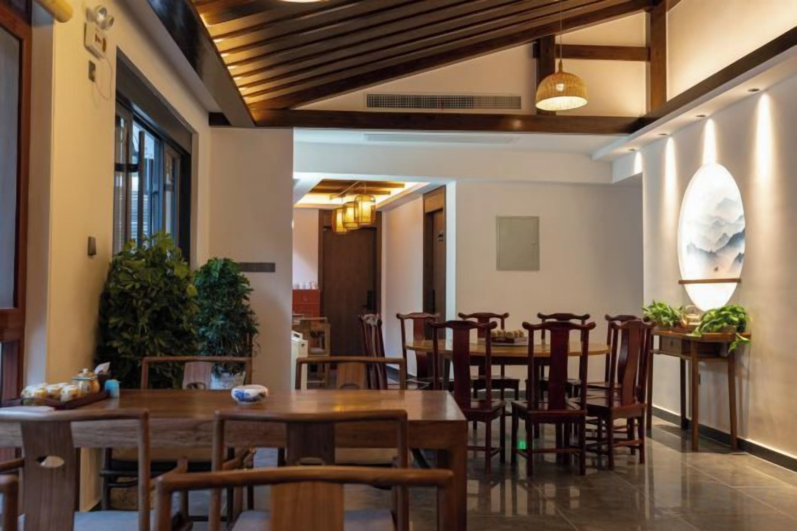 Un comedor con mesas y sillas de madera, una planta grande en maceta y una lámpara fijada a la pared.