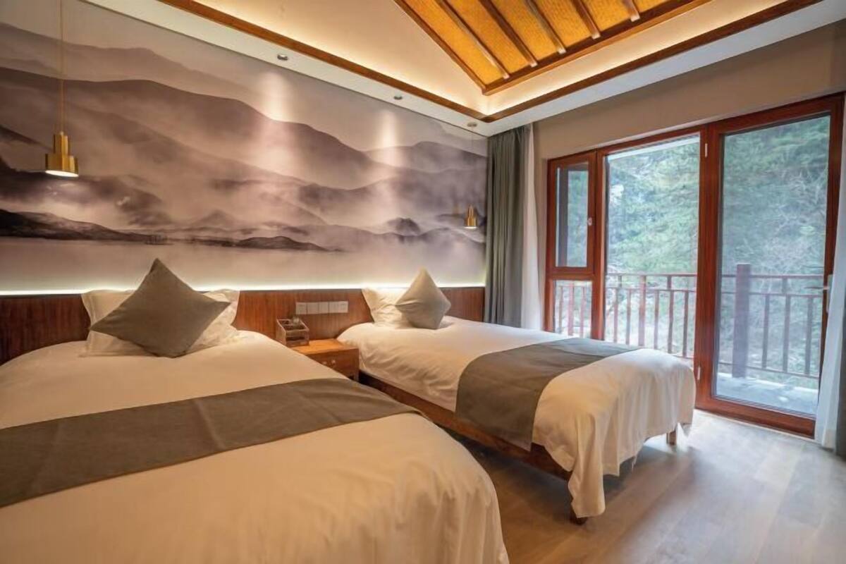A hotel room with two beds, a large window, and a mural on the wall.