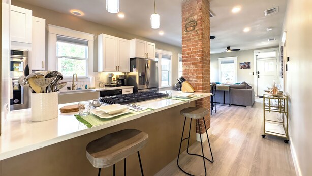 A modern kitchen with white cabinets, a stainless steel refrigerator, and a brick accent wall. - King William Charm 2-bedroom house in welcoming San Antonio with AC (San Antonio)