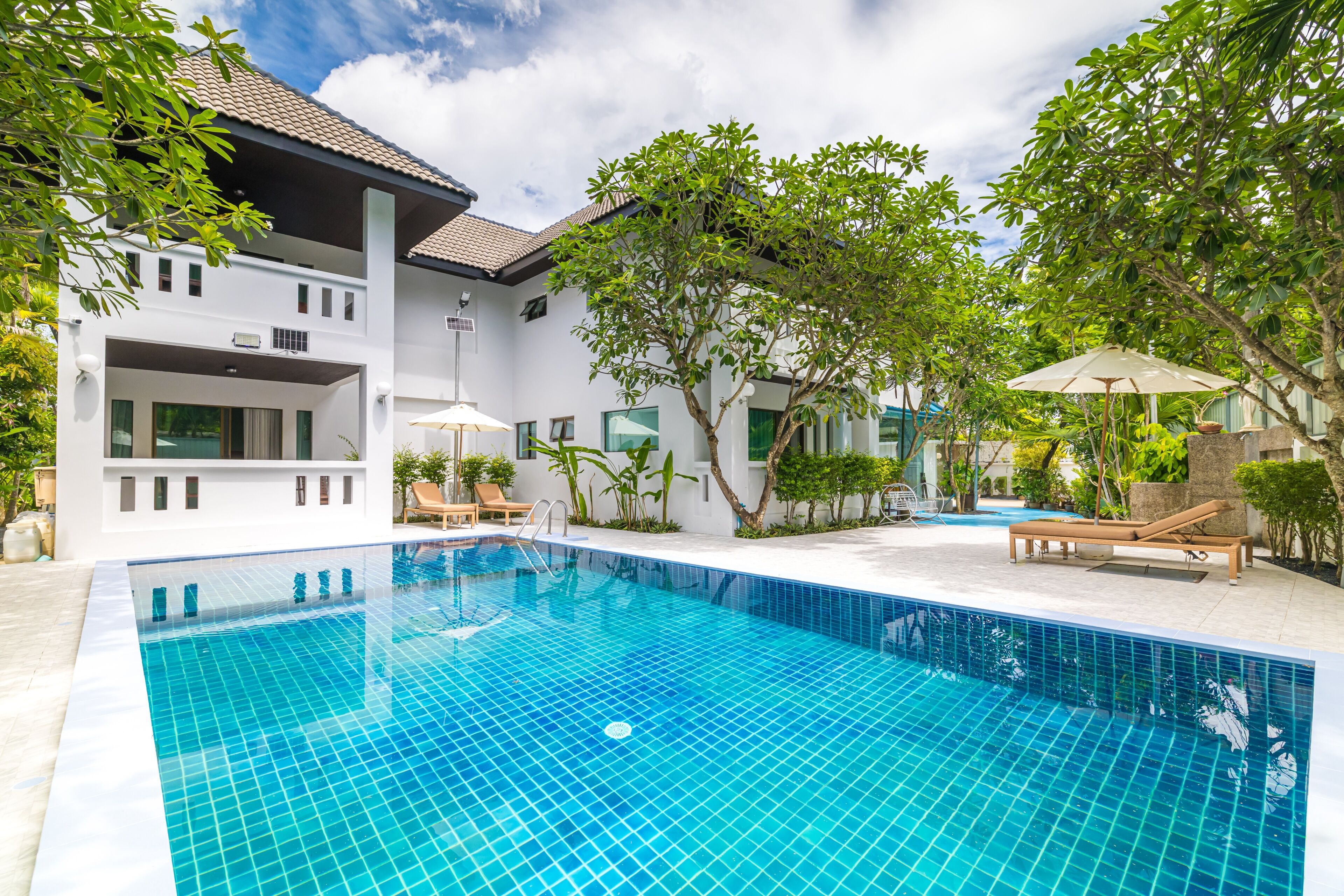 A swimming pool with a tiled deck, lounge chairs, and a building with a balcony.