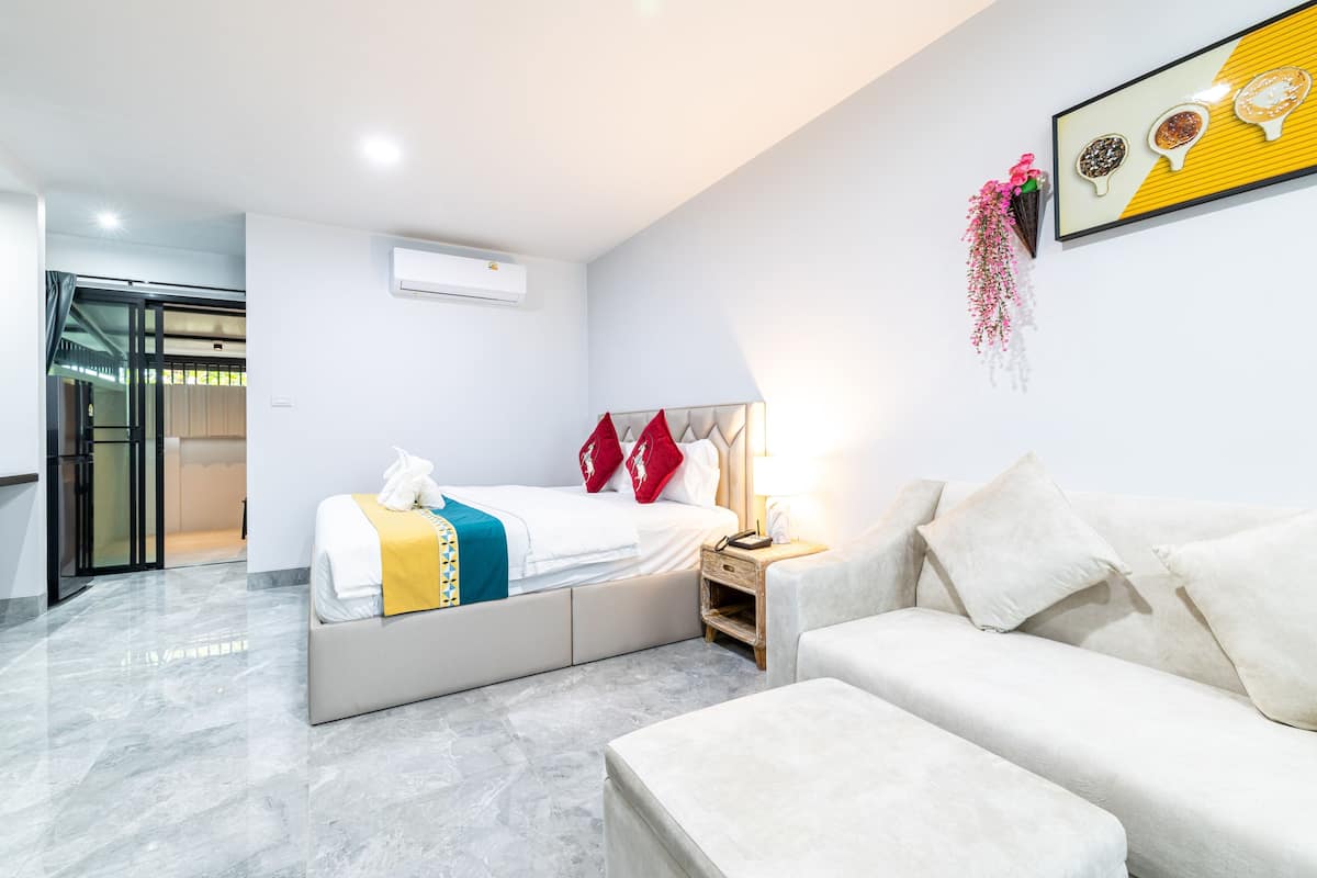 Et moderne hotelværelse med en seng, en sofa, et natbord og en vægmonteret aircondition.