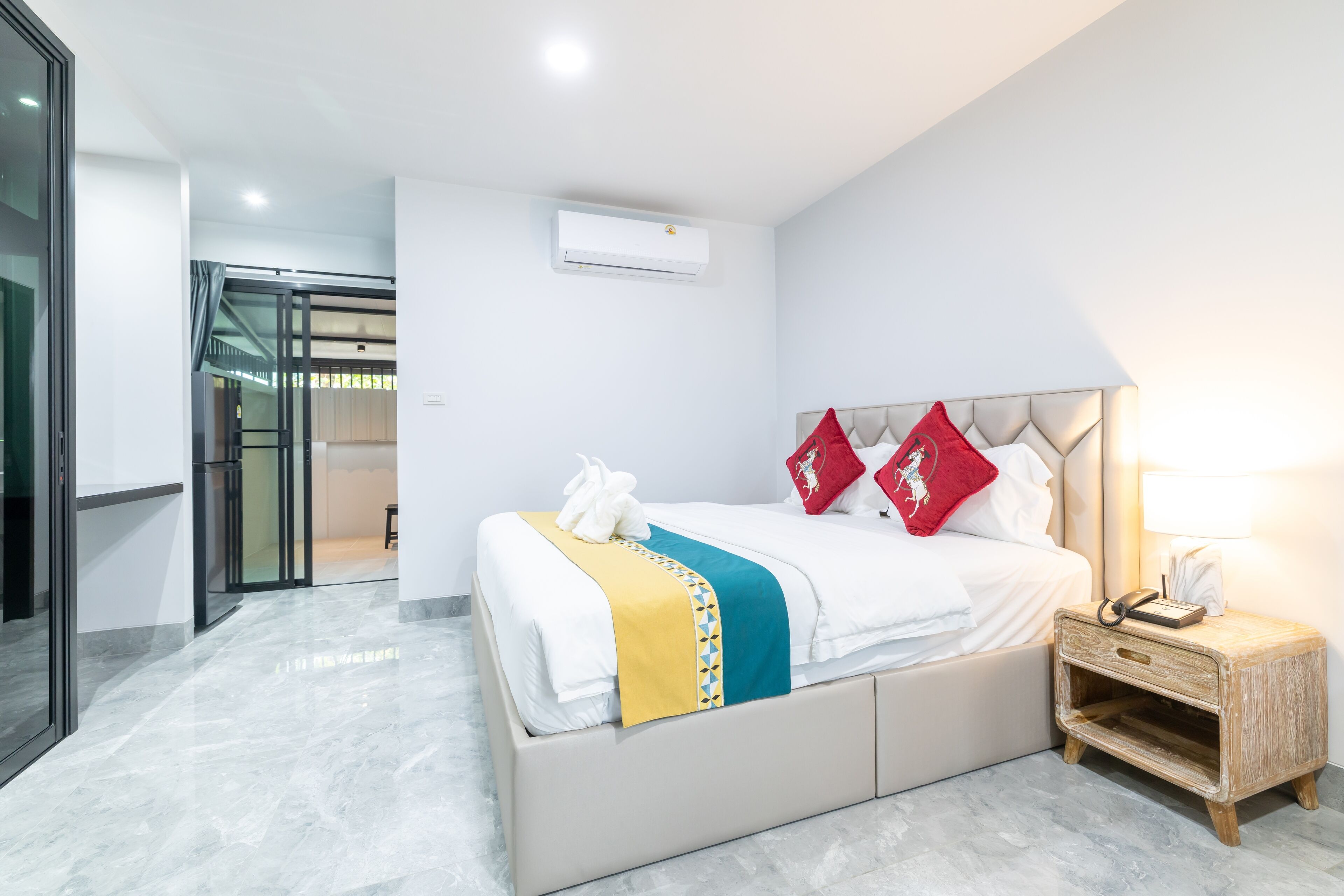 A modern hotel room with a bed, bedside table, and an air conditioning unit.