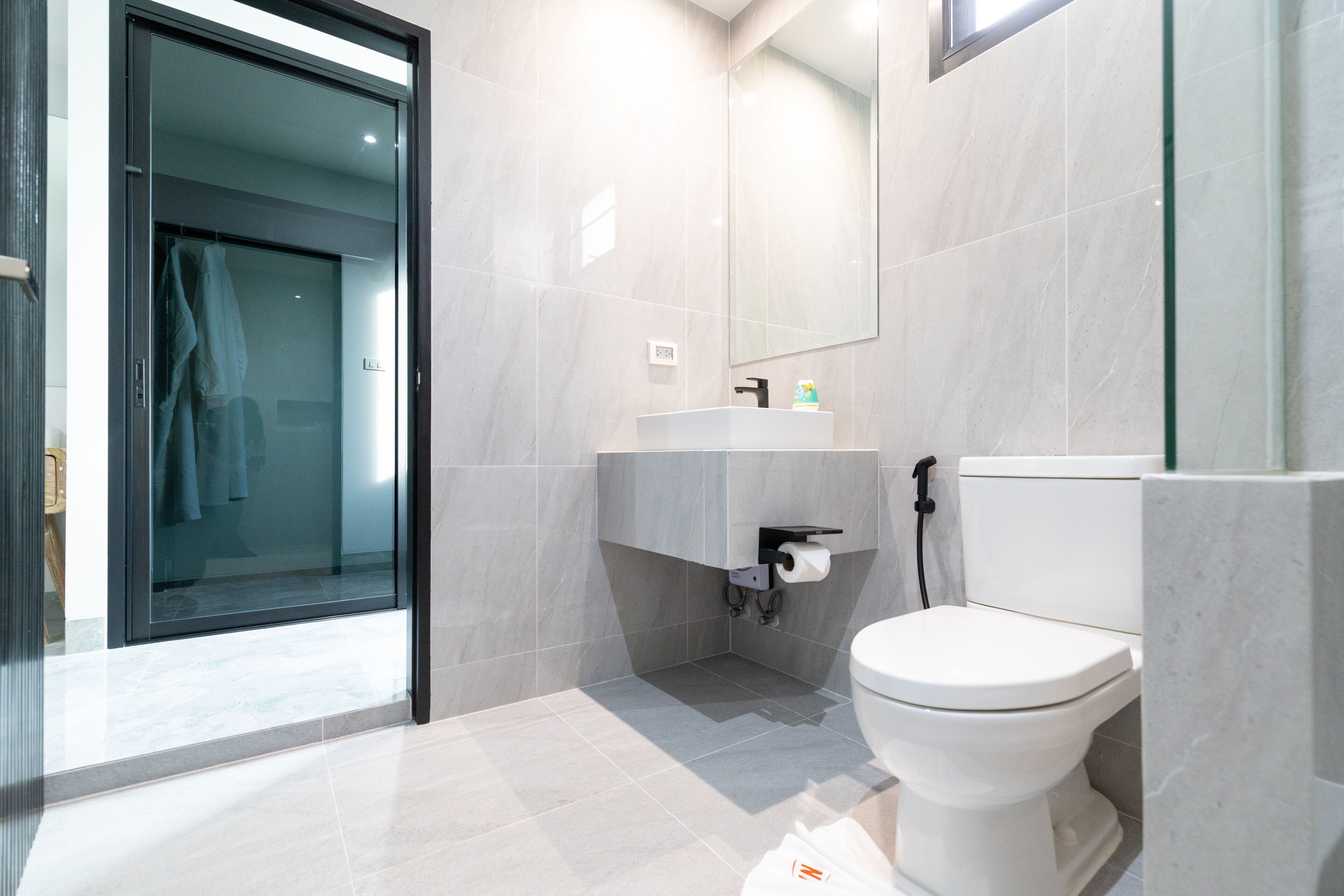 A modern bathroom with a glass shower enclosure, a white toilet, and a marble-tiled sink area.