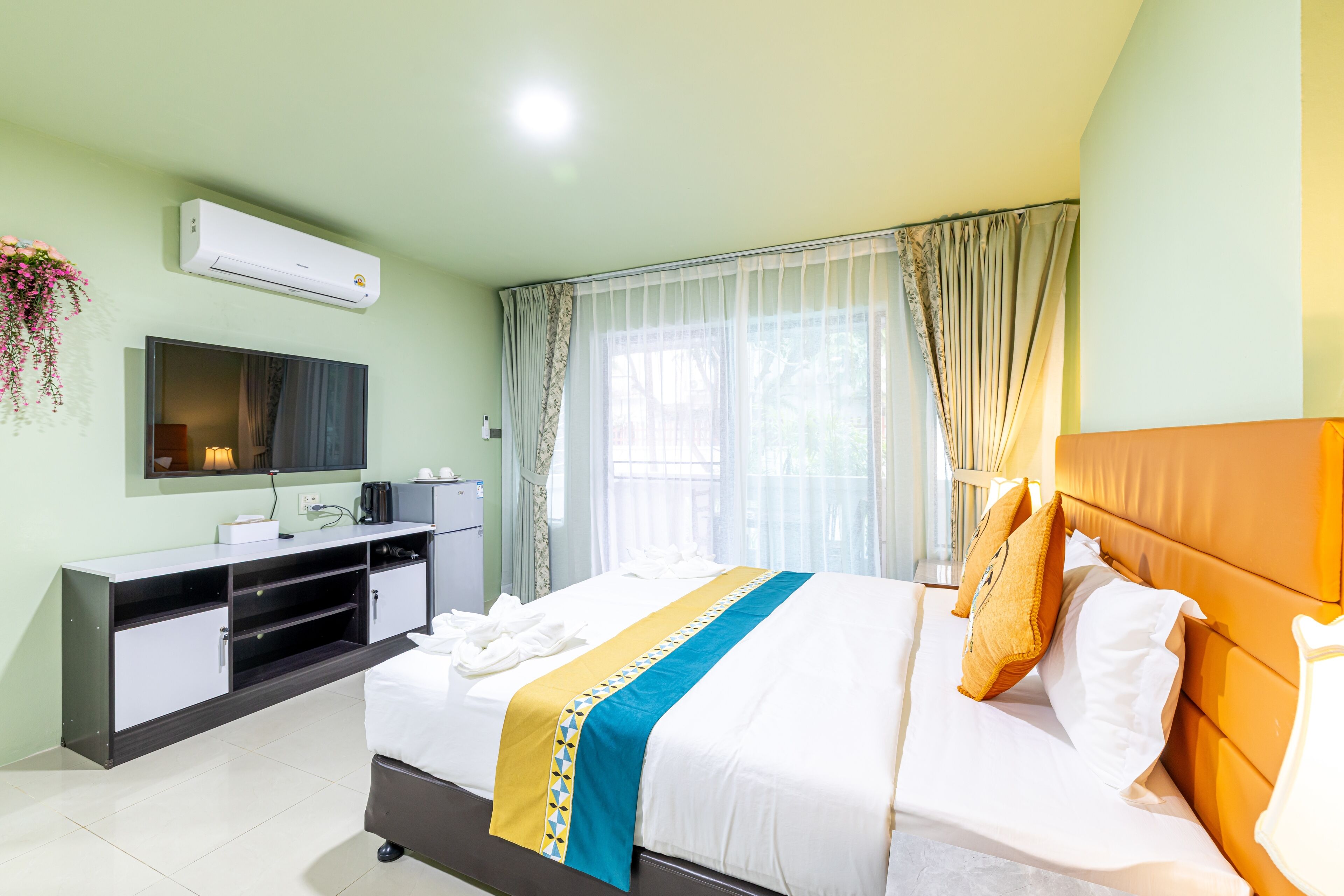 A hotel room with a bed, a TV, a desk, and a window with curtains.