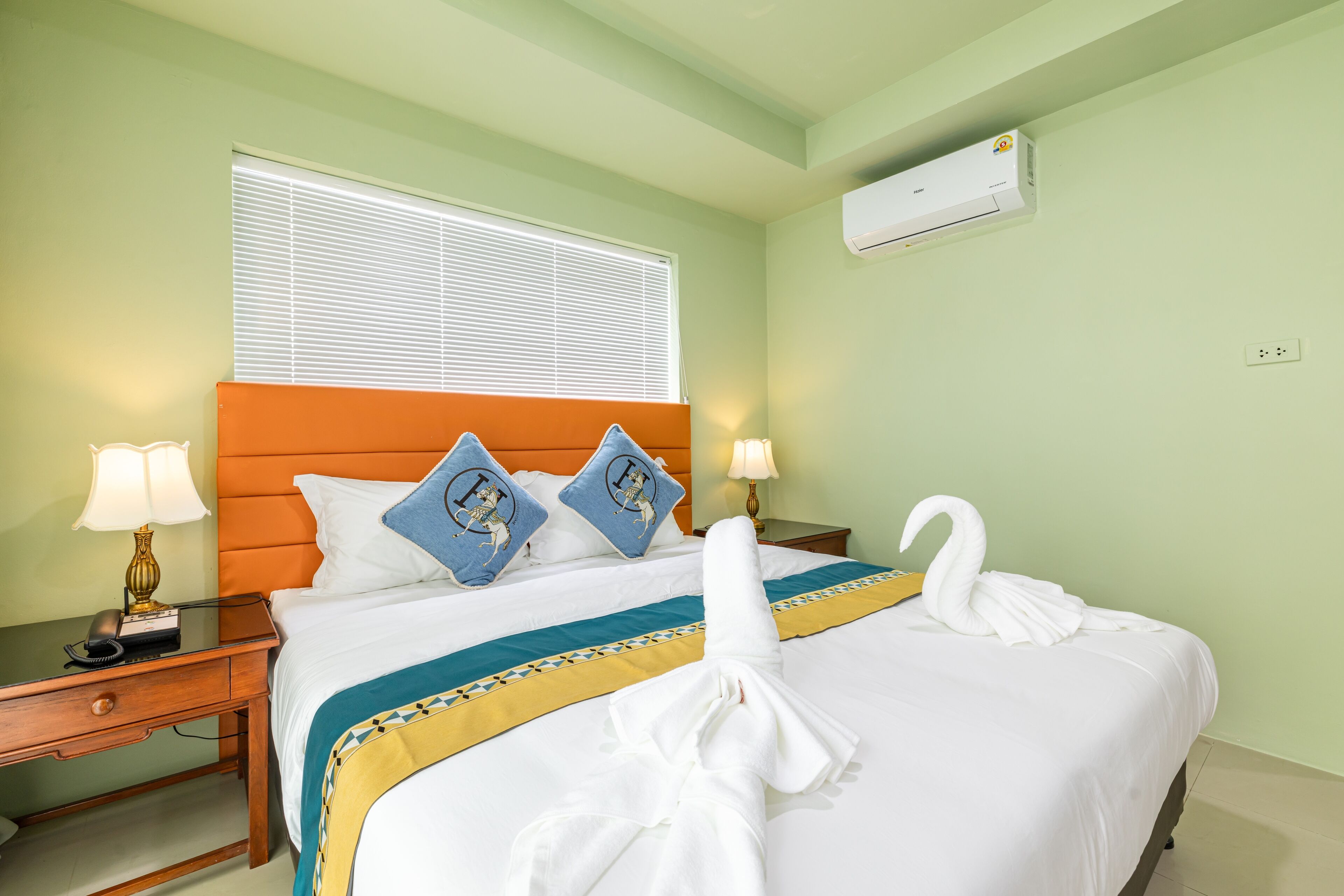 A hotel room with a bed, two pillows, a bedside table with a lamp, and an air conditioning unit on the wall.