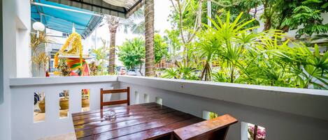Een houten tafel en stoelen op een balkon met uitzicht op een tempel en weelderige begroeiing.