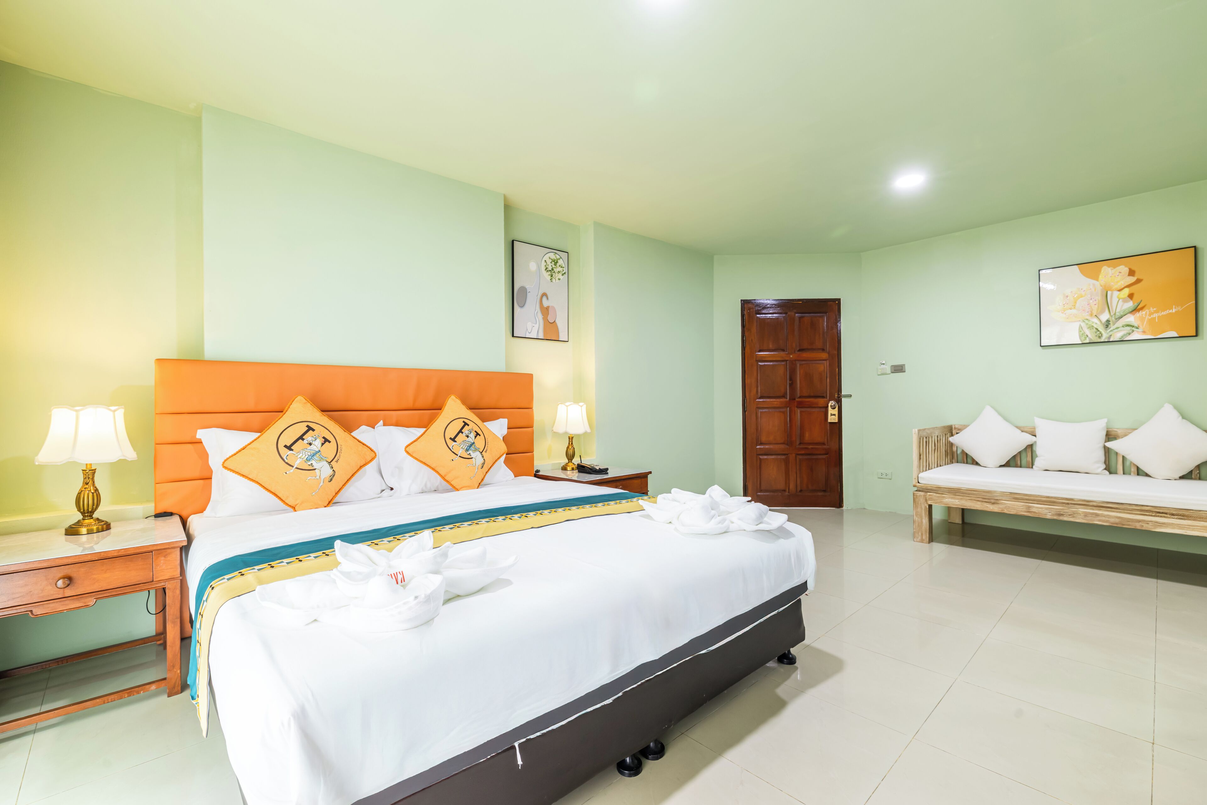 A well-lit hotel room with a large bed, a wooden bench, and a door.