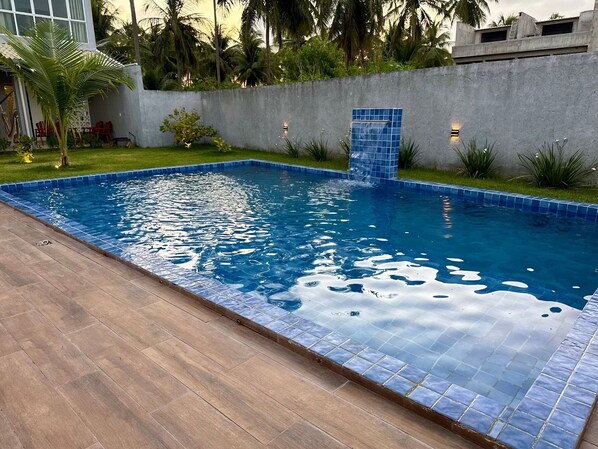 A rectangular swimming pool with blue tiles, surrounded by a wooden deck and a concrete wall. - MHV Milagres - Casa Flora (São Miguel dos Milagres)