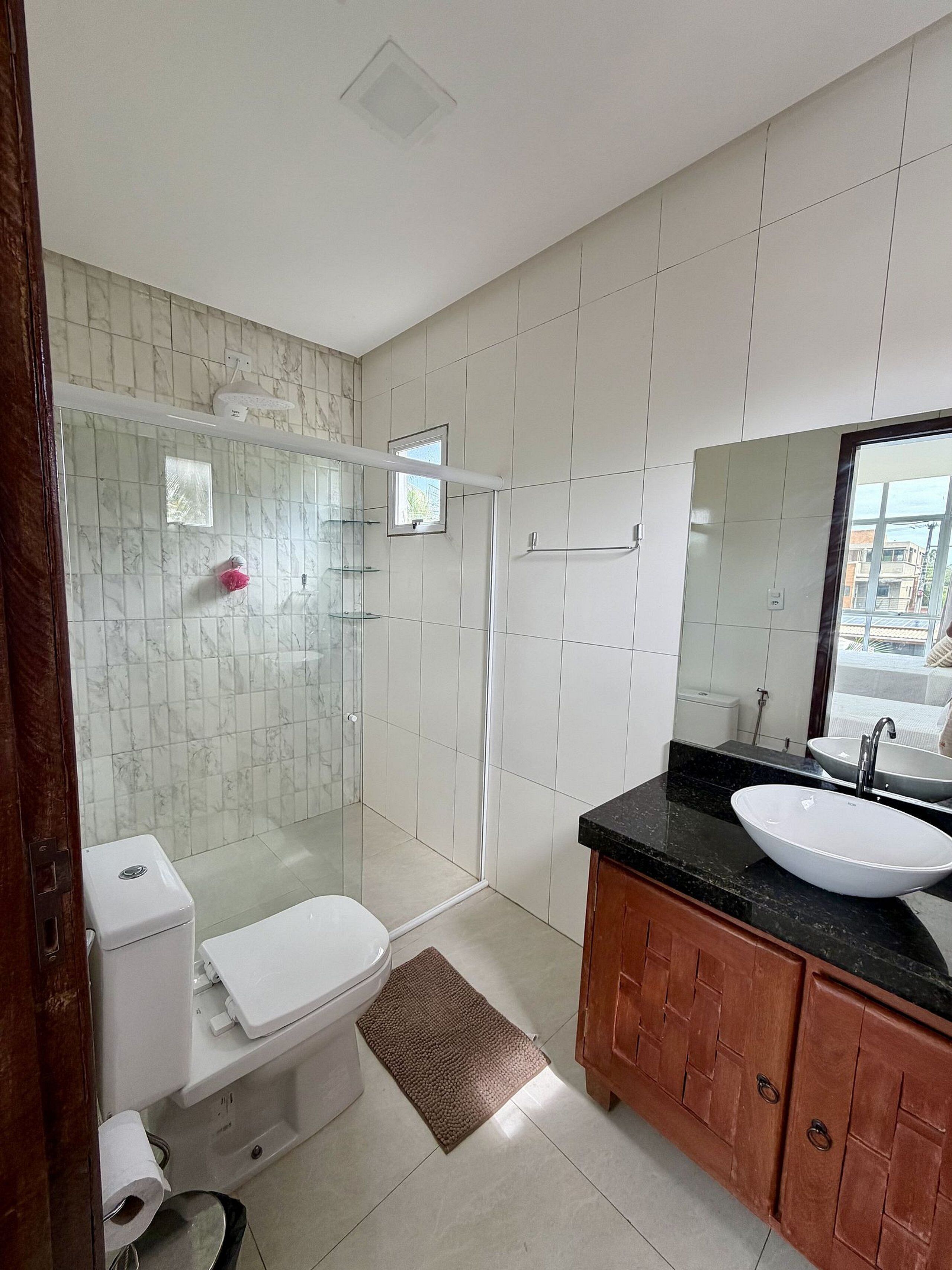A bathroom with a toilet, sink, shower, and a mirror.