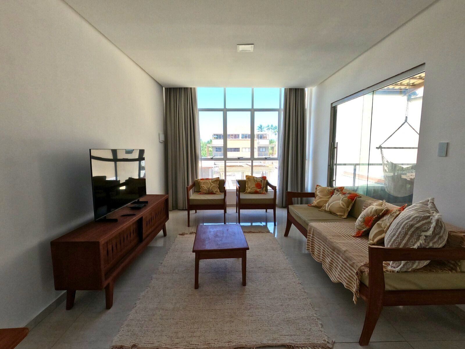 Una sala de estar con televisor, sofá, sillones y un ventanal grande.