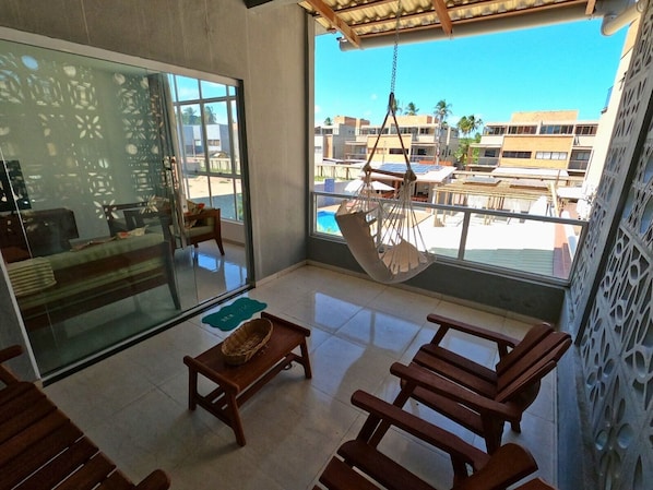 A modern room with a glass door, a hanging chair, wooden furniture, and a view of a pool and buildings.