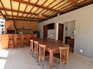 Un grand espace à manger avec une longue table et des chaises en bois, un mur en briques avec un four encastré et un téléviseur fixé au mur.