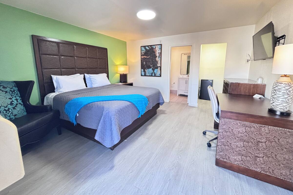 A hotel room with a bed, a desk, a chair, a lamp, and a mirror.