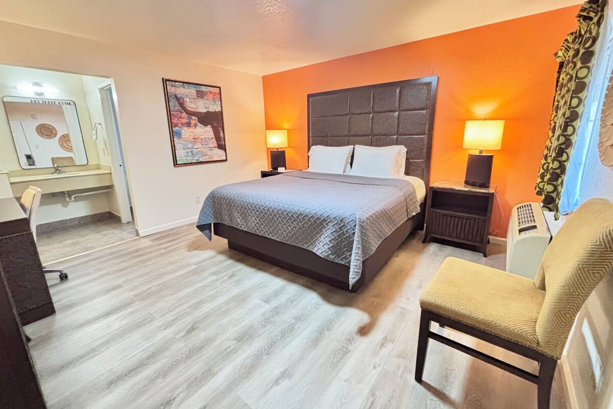 A hotel room with a bed, two bedside tables with lamps, a chair, a desk with a chair, and a mirror.