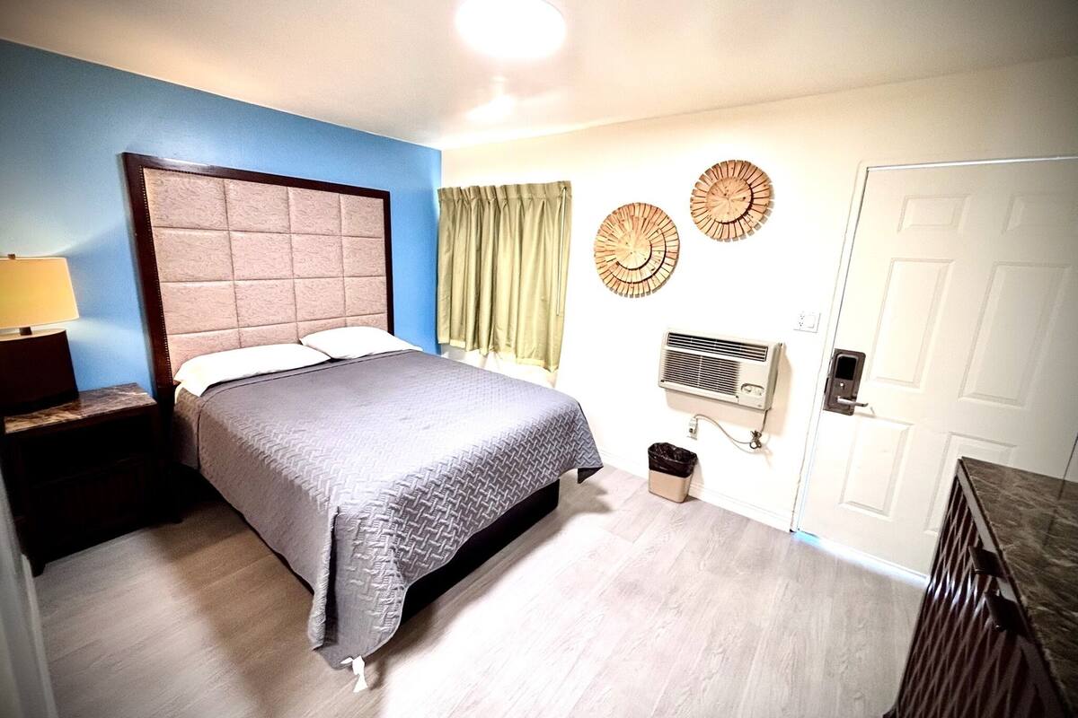 A bedroom with a bed, a nightstand, a wall-mounted air conditioner, and a door.