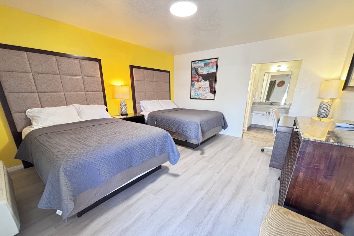 A hotel room with two beds, a desk, a mirror, and a bathroom visible through an open door.