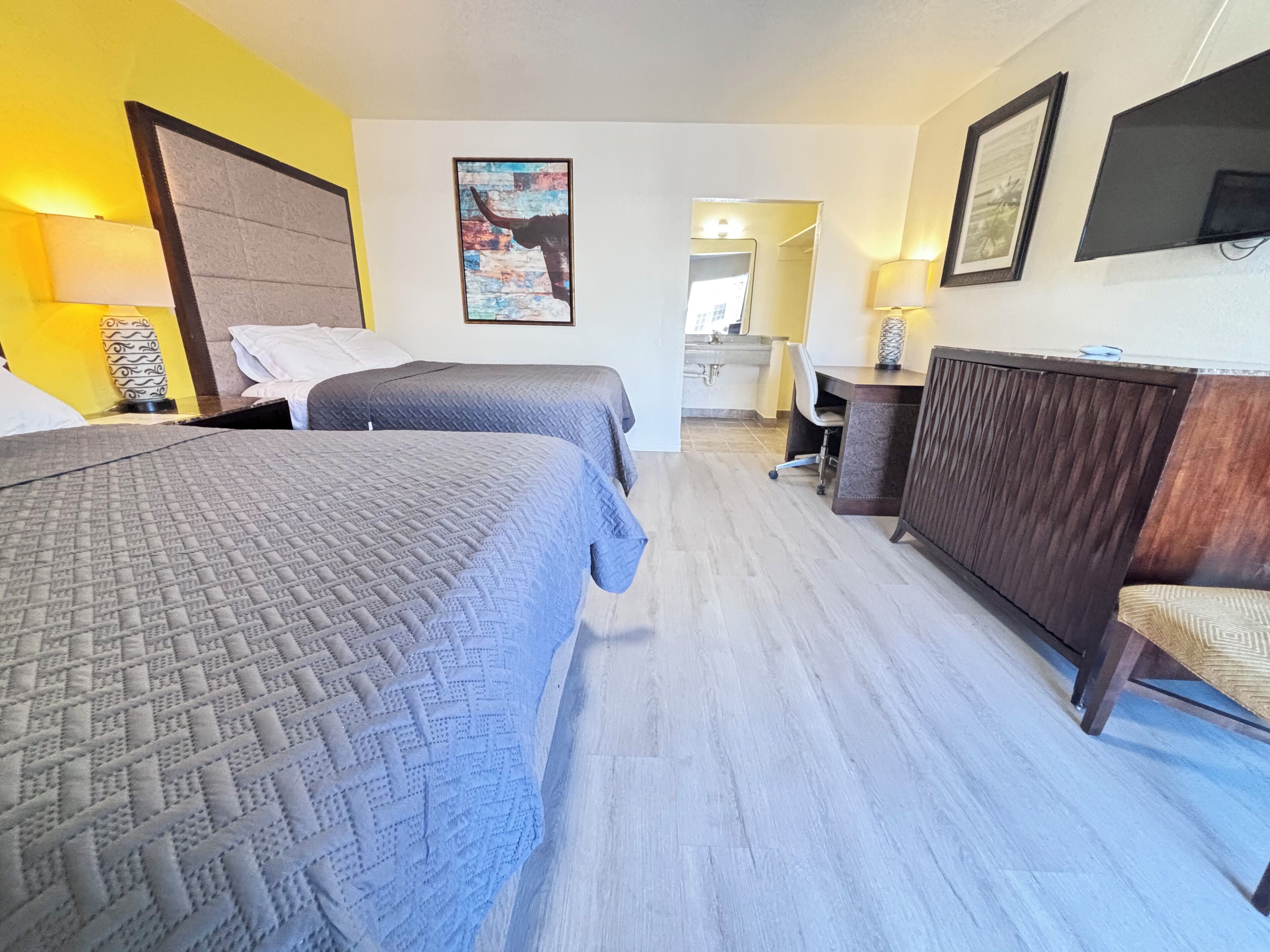 Ett hotellrum med två sängar, en byrå i trä, ett skrivbord och ett badrum som syns genom en öppen dörr.