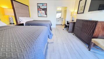 Ett hotellrum med två sängar, en byrå i trä, ett skrivbord och ett badrum som syns genom en öppen dörr.