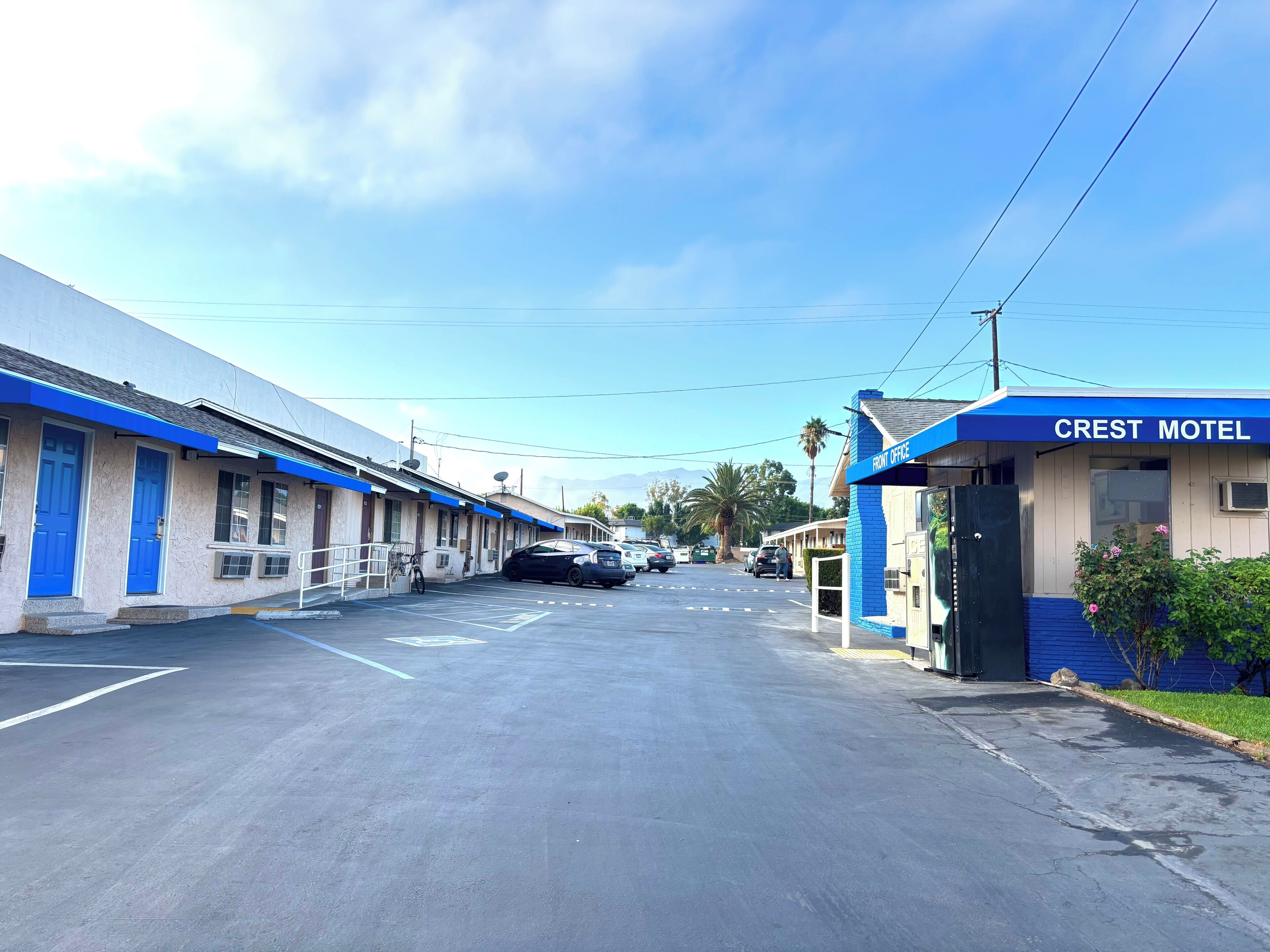 A motel with a blue awning and a sign reading 'Crest Motel.' There are parked cars and a clear sky.