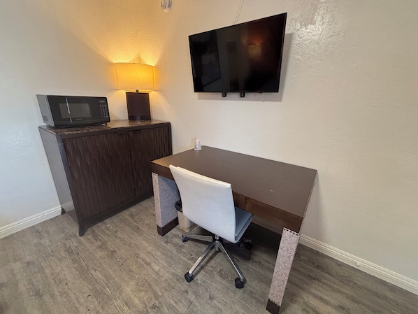 A small office space with a desk, chair, microwave, and a wall-mounted TV.