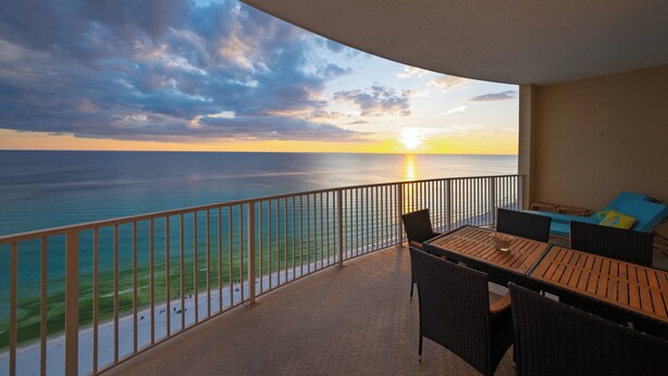 Ein Balkon mit Blick auf den Sonnenuntergang über dem Meer, ausgestattet mit einem Tisch und Stühlen.
