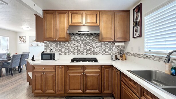 A modern kitchen with wooden cabinets, a white countertop, a built-in microwave, and a stainless steel range hood. - Entire Newly Remodeled Home With Huge Parking (Quartz Hill)
