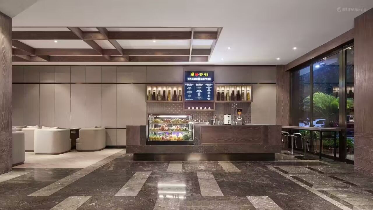 A modern hotel lobby with a central reception desk, seating area, and a large window offering a view of the outdoors.