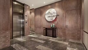 Un ascensore moderno con finiture metalliche, una parete in legno con un’opera d’arte circolare e un piccolo tavolo consolle con elementi decorativi.