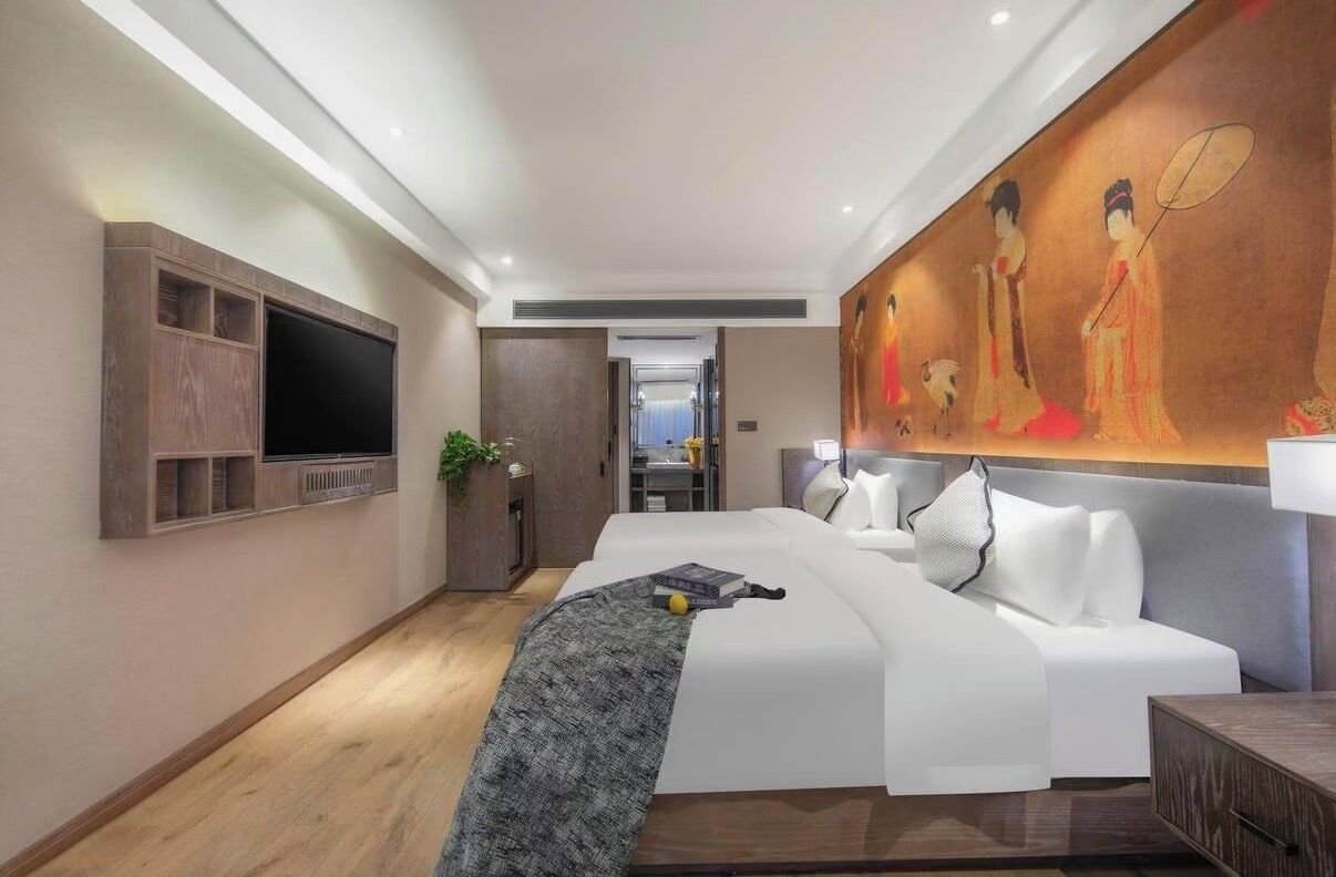 A modern hotel room with a large bed, a flat-screen TV mounted on the wall, and a large painting above the bed.