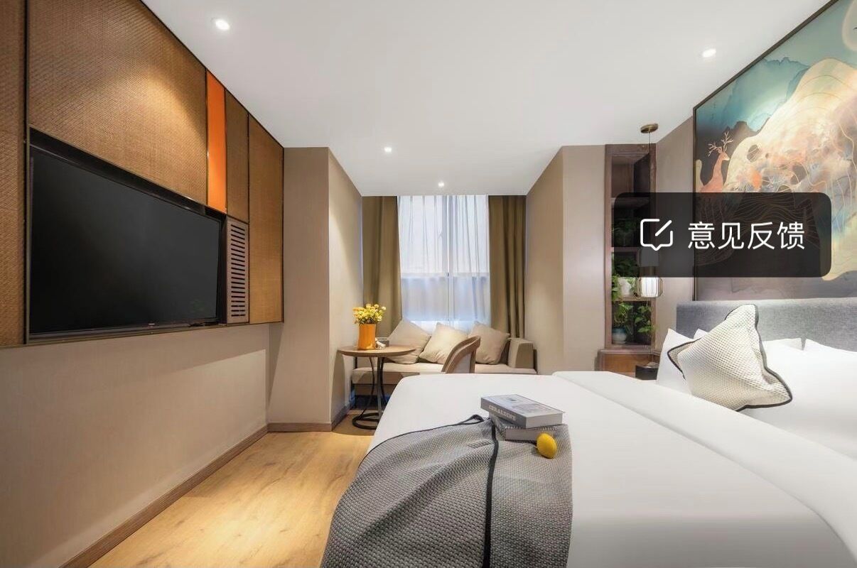 A modern hotel room with a large flat-screen TV, a comfortable bed, a small seating area with a table and chairs, and a painting on the wall.