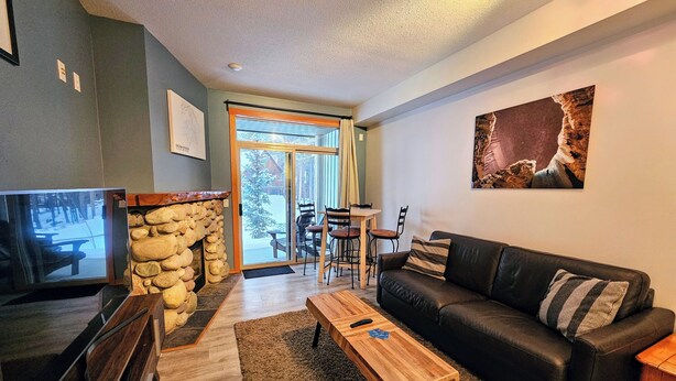 A cozy living room with a stone fireplace, a black leather sofa, and a wooden coffee table. - Rare Upper Village Townhouse w/a garage for gear and tuning! (Panorama)