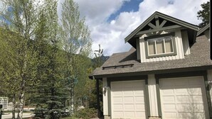 A two-story house with a garage and a small attached structure with a window. - Rare Upper Village Townhouse w/a garage for gear and tuning! (Panorama)