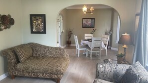 A living room with a patterned sofa, a coffee table, and a patterned armchair. There is a dining table with chairs and a chandelier in the background. - Ultra Close to the Falls (Niagara Falls)