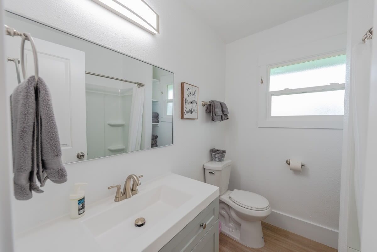 Une salle de bain moderne avec un lavabo blanc, un miroir et des toilettes. On y trouve un porte-serviettes avec des serviettes, une petite fenêtre et un panneau accroché au mur.
