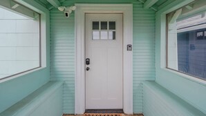 A white door with a small window above it, set in a light green building with a simple design. - Charming Modern Cottage, Downtown @pinpointstays (Coos Bay)